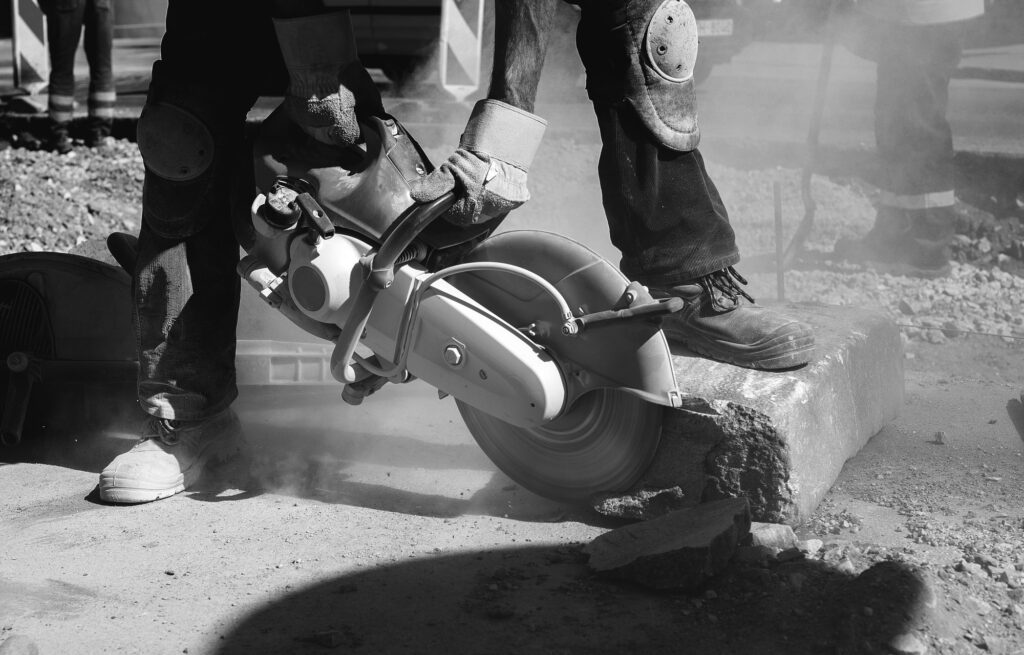 Builder worker with cut-off machine power tool breaking concrete at road construction site